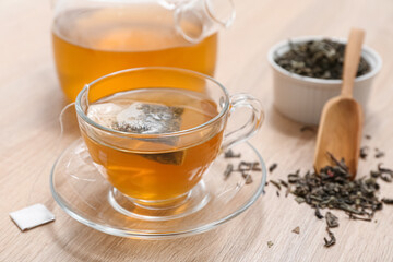 Glass cup of hot green tea and dried leaves on wooden background