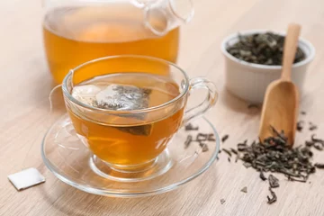 Fototapeten Glass cup of hot green tea and dried leaves on wooden background © Pixel-Shot