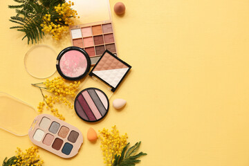 Decorative cosmetics with makeup sponges and mimosa flowers on yellow background