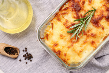 Baking dish with tasty pasta, rosemary, peppercorns and jug of oil on napkin