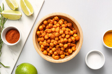 Bowl of tasty fried chickpeas with lime and spices on grey background