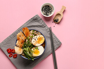 Bowl of ramen noodle soup with chicken and cucumber slices on pink background