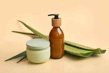 Bottle of cosmetic product and jar of cream with aloe vera leaves on beige background