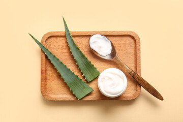 Jar and wooden spoon of cosmetic cream with aloe vera leaves on beige background