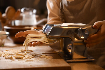 Young woman making pasta with machine at table in dark kitchen, closeup