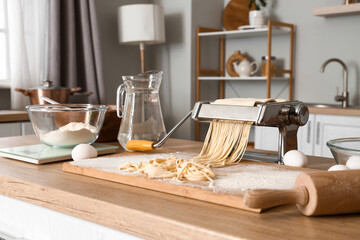 Pasta machine with dough, eggs and flour on table in kitchen