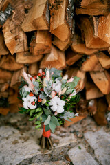 Bright wedding bouquet stands on a tile near a stack of firewood