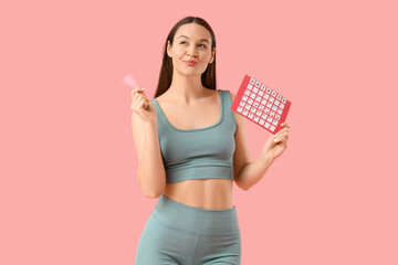 Thoughtful sporty young woman with menstrual calendar and cup on pink background