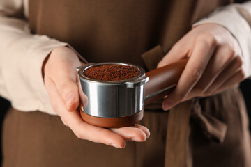 Female barista holding portafilter with coffee powder, closeup