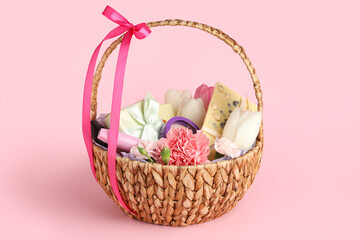Wicker basket with beautiful spring flowers, gift box, chocolate bar and cosmetics on pink background