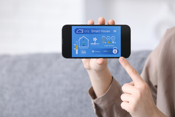 Young woman pointing at smart home security system control panel on mobile phone in room, closeup
