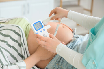 Lying pregnant woman and doctor with fetal doppler listening to baby's heartbeat in clinic, closeup