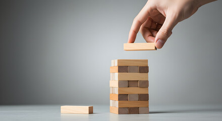 Hand Carefully Placing Wooden Block Atop Tower Game for Strategic Growth and Stability Under Studio Lighting
