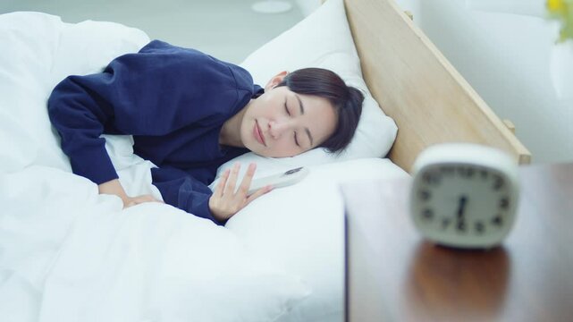 ベッドでスマートフォンを操作する女性