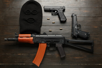 Balaclava with weapon and bullets on dark wooden background