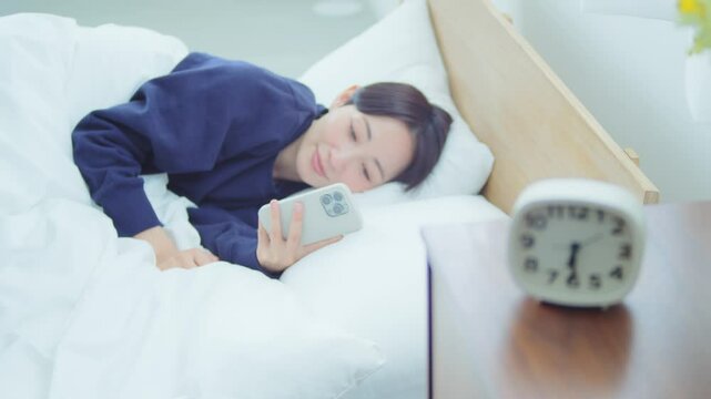 ベッドでスマートフォンを操作する女性