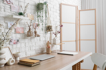 Workplace with blossoming branches and pin board on white brick wall in office
