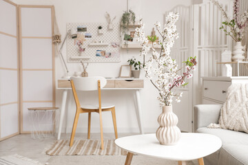 Vase with blossoming branches on table in light office