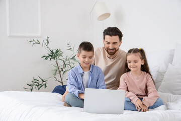 Happy father with his little children watching cartoons on laptop in bedroom