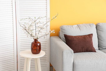 Interior of stylish living room with grey sofa, folding screen and blooming tree branches on coffee...