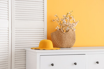 Folding screen and blooming tree branches on dresser near orange wall