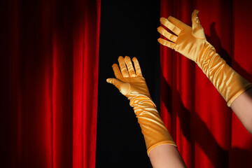 Female hands in gloves and open red curtains on black background