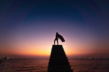 Strong woman concept. Silhouette of a young free powerful woman wearing a waving cloak standing...