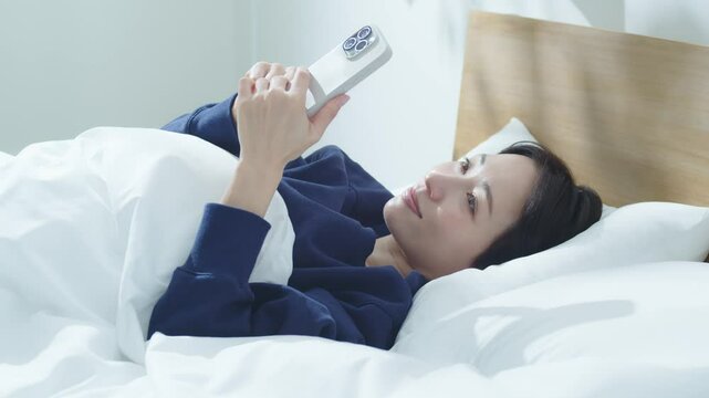 ベッドでスマートフォンを操作する女性