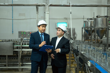 Factory supervisors in safety helmets examining a conveyor belt with metal cans in production plant