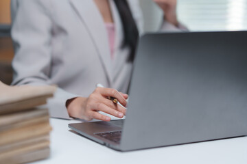 Businesswoman working diligently at a desk, using a laptop surrounded by a stack of folders. Focusing on tasks while leveraging technology for efficient business operations