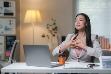 Young businesswoman is practicing deep breathing exercise at workplace desk with laptop, relieving stress from work, meditation and mindfulness, promoting mental health and well-being