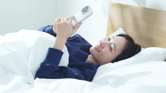 ベッドでスマートフォンを操作する女性