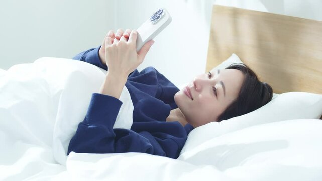 ベッドでスマートフォンを操作する女性