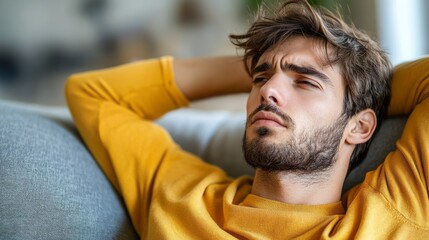 Pensive man relaxes on a sofa with hands behind head