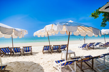 Rayong, Thailand - April, 01, 2025 :Pristine white sandy beach with rows of colorful deck chairs and umbrellas under a clear blue sky, people enjoying the ocean at Koh Samet, Rayong, Thailand