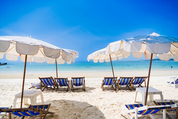 Rayong, Thailand - April, 01, 2025 :Pristine white sandy beach with rows of colorful deck chairs and umbrellas under a clear blue sky, people enjoying the ocean at Koh Samet, Rayong, Thailand