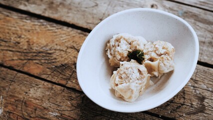 Delicious steamed dumplings in a white bowl on a rustic wooden table.  Perfect for food blogs, menus, and recipe websites.