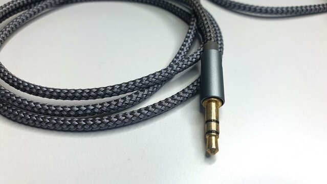 Close-up of a braided grey audio cable with a 3.5mm gold-plated connector.  Ideal for technology, music, and audio-related projects.