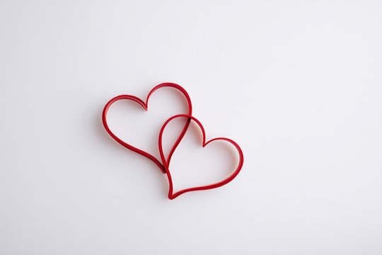 minimalistic arrangement of two intertwined red hearts on white background