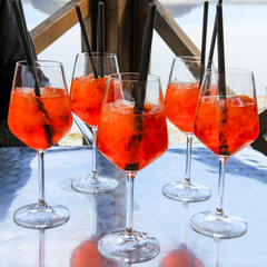 Aperol Spritz glasses with ice and straws on an outdoor table.