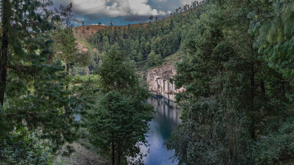Fototapeta premium A beautiful alpine lake in the crater of an extinct volcano. Steep shores. Coniferous forest on the mountainside. Reflection on calm water. Trees in the foreground. Madagascar. Tritriva Lake.