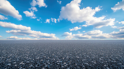 wide angle view of asphalt ground under bright blue sky filled with fluffy clouds, creating serene and expansive atmosphere. scene evokes sense of tranquility and openness