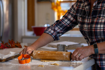 Woman rolling out sugar cookie dough for fall shaped cookies.