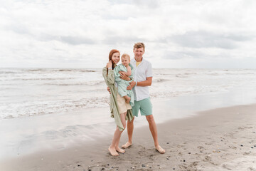Young happy family with toddler wrapped in warm blanket on beach