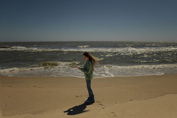 Beautiful tween checking social media standing on beach OBX