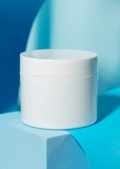 White cosmetic jar on a blue stand on a blue background. Cosmetics, science and medicine. Background for the cosmetics industry.