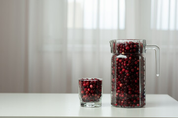 Cranberry. Small forest red berry. Cranberries in a jug and in a glass on the table. A glass of cranberries. Vitamins from nature. Selective focus.