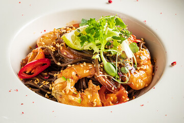 A vibrant dish featuring shrimp and vegetables on dark noodles, garnished with herbs and lime