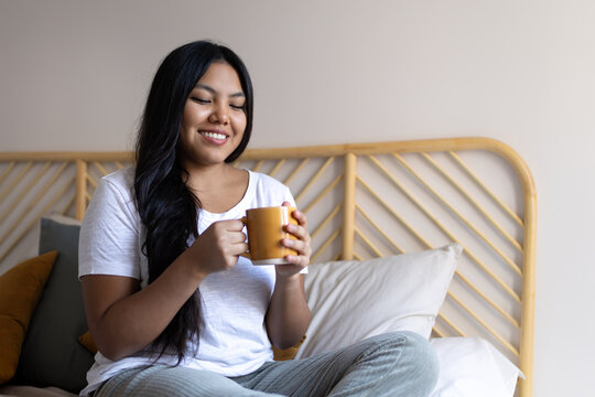 Young latin woman enjoying morning coffee in bed - Powered by Adobe