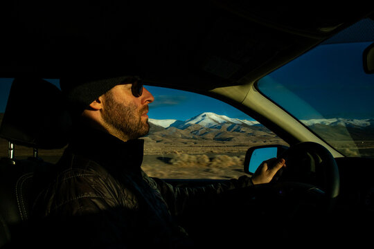 Man driving with snow-capped mountains outside truck window.